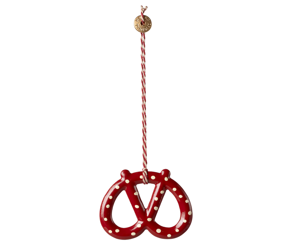 The Maileg Christmas Metal Ornament - Pretzel - Dot is a red, hand-painted pretzel-shaped ornament with white dots, hanging from a red-and-white striped string with a small gold disc—perfect as a charming Christmas tree decoration.
