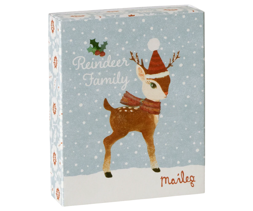 A holiday-themed gift box featuring adorable metal ornaments of the Maileg Reindeer Family illustrated with a cute reindeer wearing a red Santa hat and scarf, adorned with holly accents and snowflakes. The text includes "Reindeer Family" and "Maileg," while the light blue background enhances its festive charm.