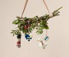 A handmade Christmas tree decoration showcasing a collection of greenery and pinecones adorned with four Maileg ornaments, including the Maileg Guard Ornament in red, a heart, a duck, and a small round design. Each ornament is crafted in festive colors.