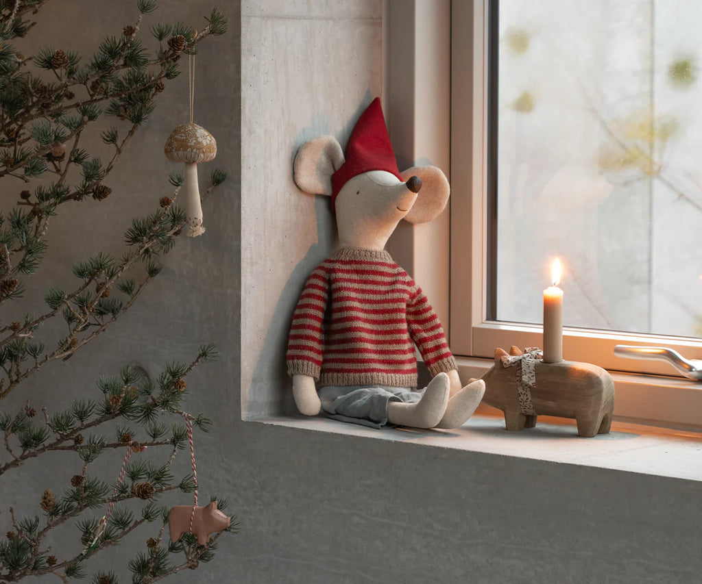 The PRE-ORDER: Maileg Christmas Mouse, Maxi - Boy (Estimated Arrival Early September) in a red striped sweater and hat sits by a lit candle and wooden hippo on a windowsill, with pine branches and ornaments on the left.