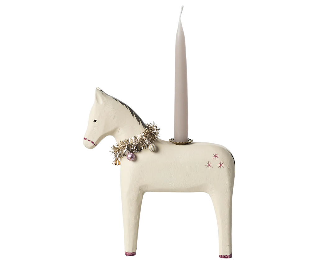 The Maileg Wooden Horse Candle Holder - Small is a charming decorative piece shaped like a white horse. It features a tinsel garland and small ornaments around its neck. A candle sits vertically on its back, perfect for creating a cosy Christmas atmosphere, while pink accents highlight the hooves and simple star designs embellish its body.