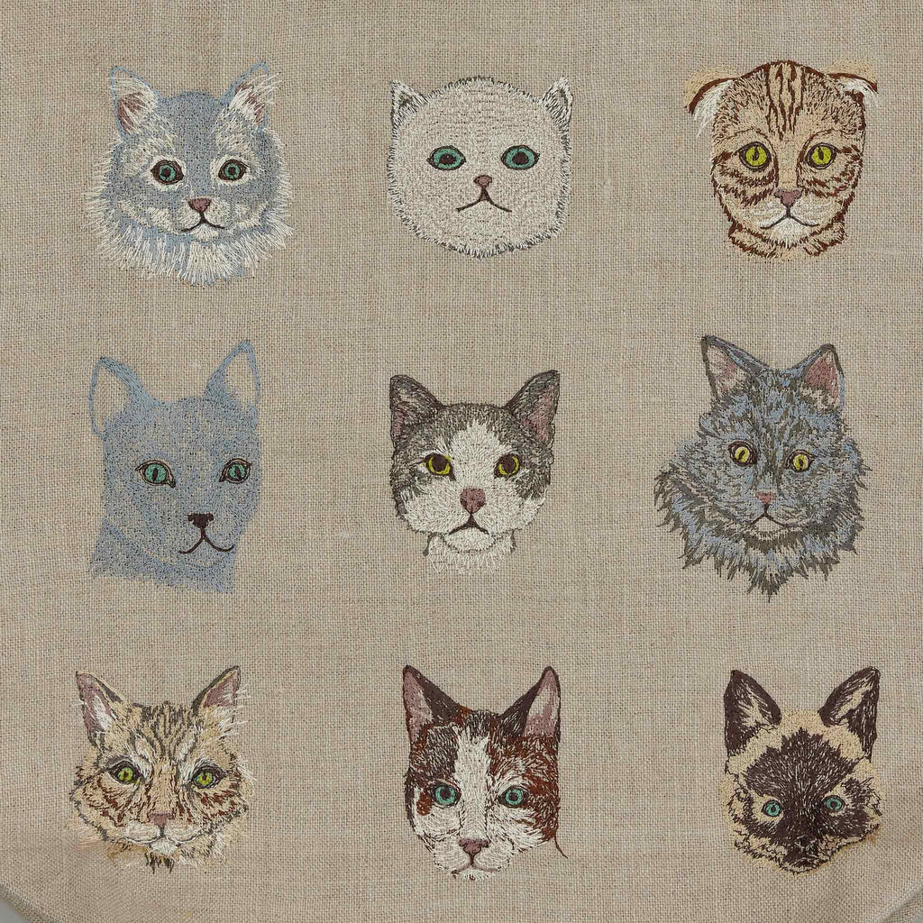 The Cats Tote Bag features a 3x3 grid of nine embroidered feline faces, each with unique colors and expressions on a beige background, showcasing varied fur patterns and eye colors for added charm.