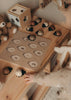 A child reaches for the My Little Lady Bug Wooden Puzzle on a small table, with a teddy bear and wooden peg puzzle shape sorter nearby.