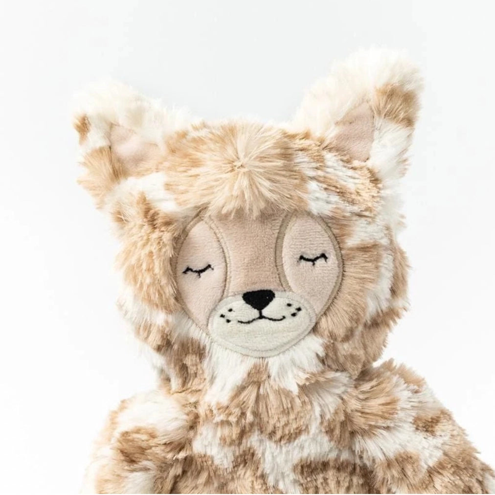 A close-up image of a Slumberkins Lynx Kin + Lesson Book On Self Expression, with a soft beige and brown fur pattern, stitched eyes closed in a peaceful expression, and tufted ears.