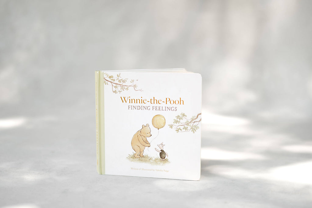 The board book Winnie-the-Pooh: Finding Feelings stands upright on a light surface, featuring Pooh with a balloon talking to Piglet about emotions for toddlers.