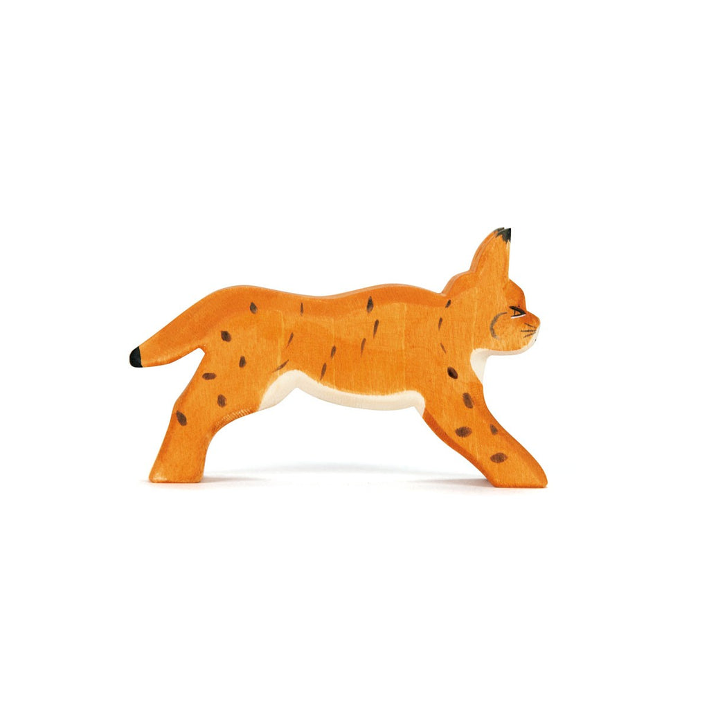 The Ostheimer Lynx Running is a handcrafted wooden toy lynx, painted in orange with black spots and detailed features. It stands with its back legs and front legs apart as if mid-step. The lynx has pointed ears, and its tail and facial details are painted black. Made from sustainably sourced materials, the background is white.