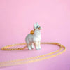 A delicate, handcrafted Alpaca Necklace featuring a 24k gold chain and a small, white alpaca pendant. The soft pink background enhances its charming and whimsical appearance. Intricate details on the pendant add a playful touch to the elegant jewelry piece.