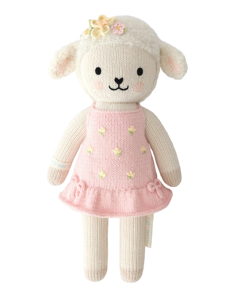 Cuddle + Kind Eleanor the Lamb is a hand-knit, fair trade doll from Peru, featuring a friendly lamb in a pink dress with yellow and floral accents, black eyes, a small nose, and a gentle smile.