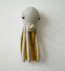 A BigStuffed Octopus - Pop hangs on a white wall. The octopus is light gray with yellow underside detailing on its eight long fluffy tentacles. The toy's eyes are green, giving it a gentle and whimsical appearance, as if inviting you into an enchanting underwater world.