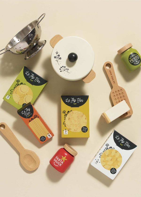 The Pretend Play Pasta Set encourages imaginative play with a strainer, pot, spaghetti boxes, cheese block, grater, wooden spoon, pesto jar, and pasta sauce jar—all perfectly arranged on a light surface for unlimited culinary adventures.