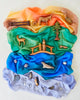 The Sarah's Silk Enchanted Playsilk in Ocean serves as the blue sea, while wooden animal figures, trees, and rocks are placed on corresponding sections of colorful draped playsilks to inspire imaginative play and demonstrate various ecosystems.