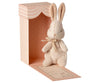 A plush beige Maileg Bunny Easter Basket Set with a bow around its neck, standing in front of a pink striped box with a pastel orange interior. The box has a bow illustration and text at the bottom