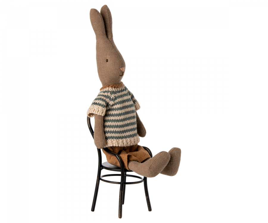 A Maileg Rabbit Size 1 - Brown - Shirt And Shorts is seated on a small metal chair, perfect for the Maileg dollhouse. The rabbit is upright, with its legs extended outward and its ears pointing upward against a plain white background.