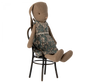 A seated Maileg Bunny, Size 1, Brown - Blossom Dress made from Maileg fabric and wearing a floral-patterned dress. The Maileg Bunny, Size 1, Brown - Blossom Dress features long ears and is positioned on an ornate black metal chair. The toy has a simple, hand-crafted appearance with a rustic, decorative style, utilizing recycled polyester for added eco-friendliness.