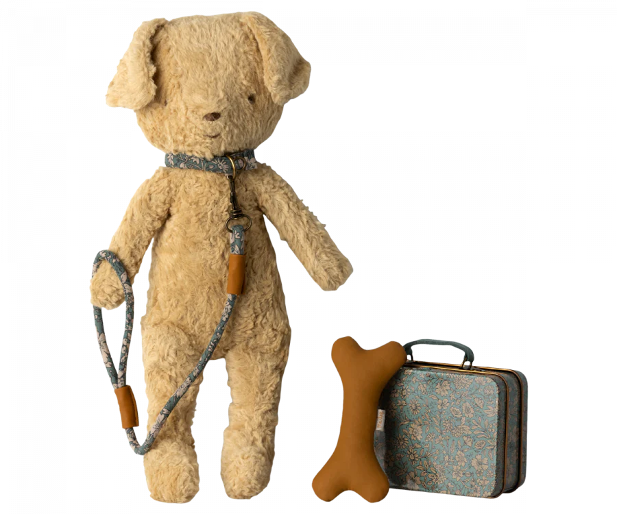 A Maileg Puppy Accessories - Blue stands upright. Beside it are a beige bone-shaped toy and a small vintage-style suitcase with a Maileg print floral pattern.