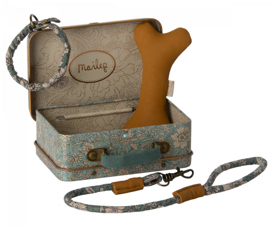 A small blue floral-patterned suitcase containing a tan bone-shaped toy and a coiled blue floral leash. The suitcase is open, displaying a beige interior with "Maileg" embroidered on the back. A matching blue floral collar and leash set is attached to the suitcase handle. The product includes Maileg Puppy Accessories - Blue.