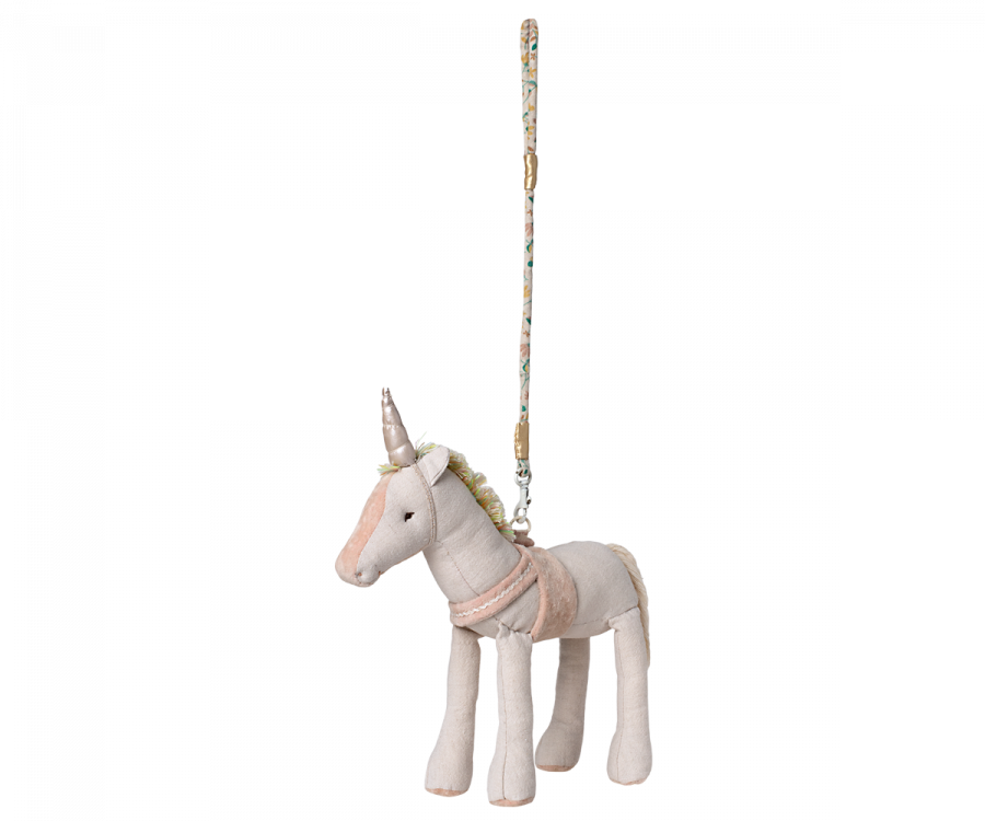 A Maileg Unicorn plush toy with a pink mane and a golden horn, attached to a wooden pole, isolated on a black background.