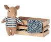 A Maileg Pig In Box, Baby - Boy toy standing next to a small wooden box filled with assorted colorful fabrics, isolated against a white background.