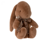 A Maileg Medium Plush Bunny, soft and fuzzy in its soft plush fabric, is sitting upright with floppy ears. It wears a beautiful bow around its neck, adding a touch of charm to its cuddly appearance.