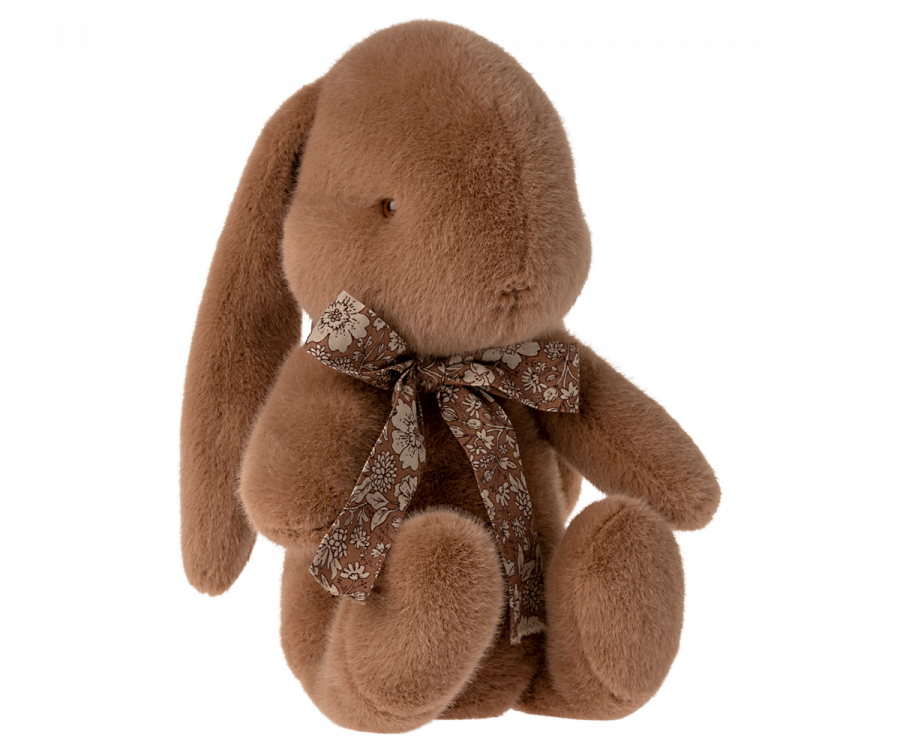 A Maileg Medium Plush Bunny, soft and fuzzy in its soft plush fabric, is sitting upright with floppy ears. It wears a beautiful bow around its neck, adding a touch of charm to its cuddly appearance.
