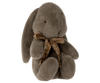 A Maileg Medium Plush Bunny with long, floppy ears is sitting upright. It has a small, brown embroidered nose and black eyes. The bunny is adorned with a beautiful bow around its neck featuring a white floral pattern, made from soft plush fabric for an extra sweet look.