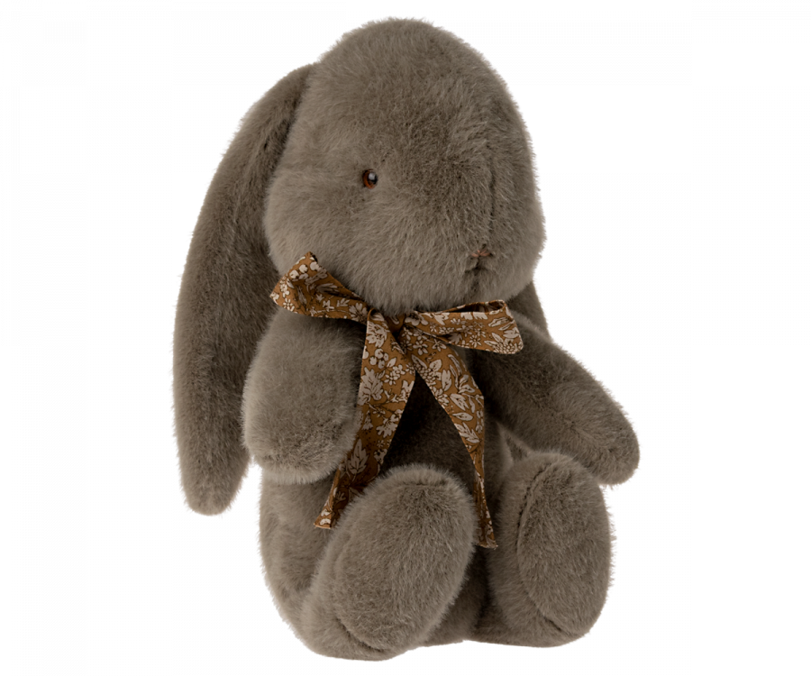 A Maileg Medium Plush Bunny with long, floppy ears is sitting upright. It has a small, brown embroidered nose and black eyes. The bunny is adorned with a beautiful bow around its neck featuring a white floral pattern, made from soft plush fabric for an extra sweet look.