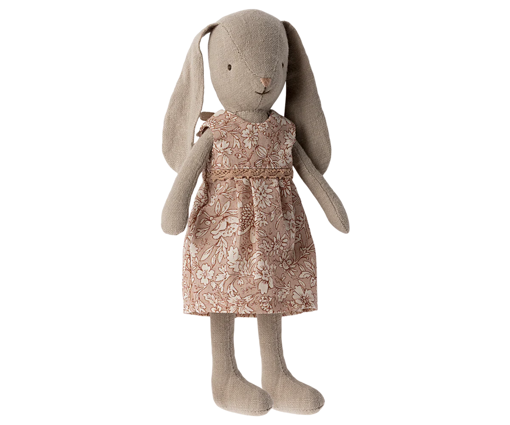 A Maileg Bunny, Size 1 - Classic Flower Dress stands upright, wearing a pink dress adorned with a white floral pattern. Made from recycled polyester, the bunny has long ears, a simple stitched face, and a gentle, neutral color.