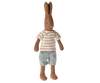 A Maileg Rabbit Size 1, Chocolate Brown - Striped Blouse and Shorts resembling a rabbit, wearing a striped white and beige shirt and light gray shorts. The toy stands upright with long ears, a simple stitched face, and is crafted from soft natural fabrics. This charming bunny wardrobe addition is perfect for any collection.