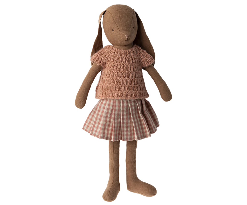 A Maileg Bunny, Size 3 - Knitted Shirt & Skirt wearing a knitted pink sweater and a checkered skirt. The rabbit, made from soft natural fabrics, has long ears and stands upright with its arms extended slightly to the sides.