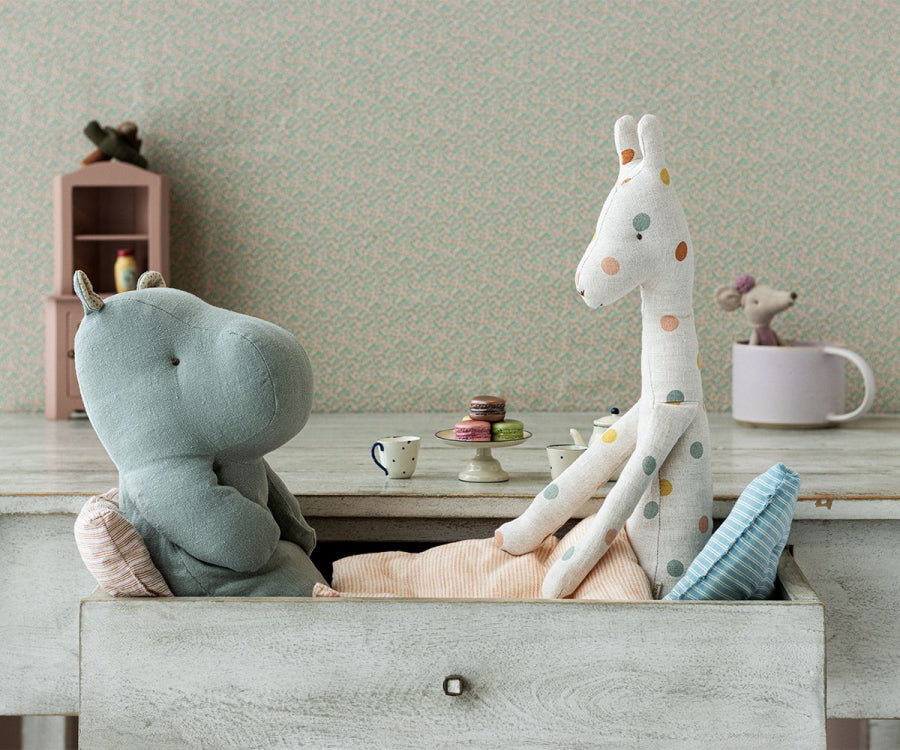 Two Maileg Medium Hippo Stuffed Animals in Chino Green, sitting at a table with miniature teacups and stacked macarons on a plate, in a cozy room with pastel wallpaper.