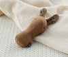 The Maileg Lullaby Friend Rattle, Bunny Rattle - Chocolate lies on a cream-colored textured blanket. This charming toy, made of soft fabrics and featuring simple stitched features and floral-patterned ears, rests on a subtly patterned beige sheet. It would make a delightful addition to any gift box.