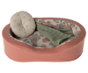 The Maileg Small Cozy Bed - Coral is a small, oval-shaped pet basket featuring a pink fabric exterior. Its interior is lined with floral-patterned fabric and includes a round cushion adorned with green polka dots, as well as a snug green knitted blanket.