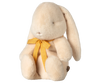 The Maileg Plush Bunny - Small Cream, available for pre-order and shipping in February, is a soft and fluffy bunny with long ears and a minimalist face. Crafted from recycled polyester, it has beige fur and wears a charming yellow bow.