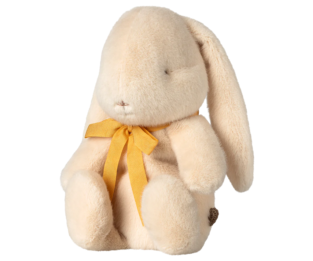 The Maileg Plush Bunny - Small Cream, available for pre-order and shipping in February, is a soft and fluffy bunny with long ears and a minimalist face. Crafted from recycled polyester, it has beige fur and wears a charming yellow bow.