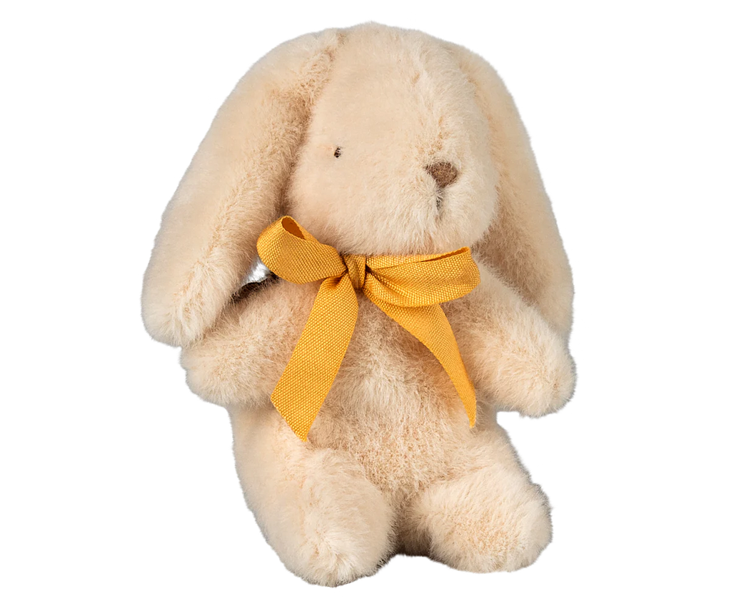 A soft Maileg Plush Bunny - Mini Cream, pre-orderable and shipping in February, sits upright. Crafted from recycled polyester, this beige bunny has floppy ears, a stitched black nose, and a bright yellow ribbon tied as a bow around its neck.