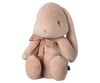 The PRE-ORDER: Maileg Plush Bunny - Medium Light Powder is a soft, eco-friendly bunny with a sweet minimalist design. It sits upright, features long floppy ears, has an embroidered face with a calm look, and is adorned with a brown ribbon. Crafted from recycled polyester, it ships in February.