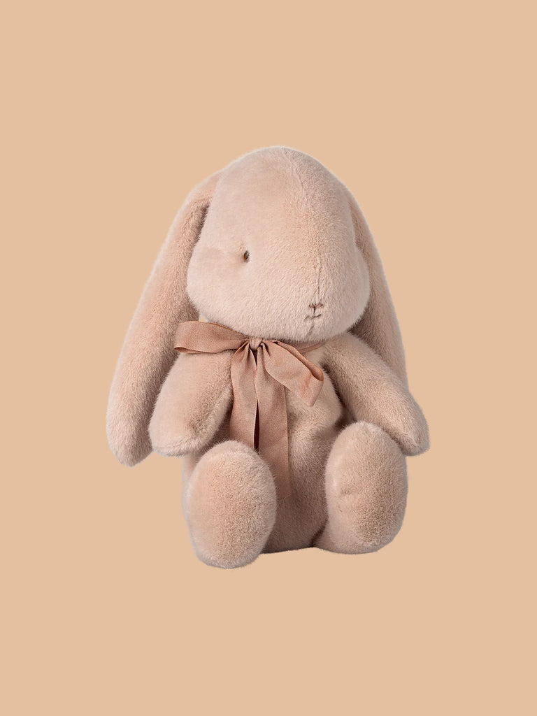 The Maileg Plush Bunny - Medium Light Powder, made from recycled polyester, features long ears and a charming design with a small smile and light brown ribbon, sitting against a plain tan background. Pre-order now for shipment in February.