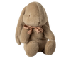 The Maileg Medium Plush Bunny in Dusty Brown features cozy fabric and polyester fillings, designed to sit upright. It boasts long ears and a charming pink ribbon adorning its neck.