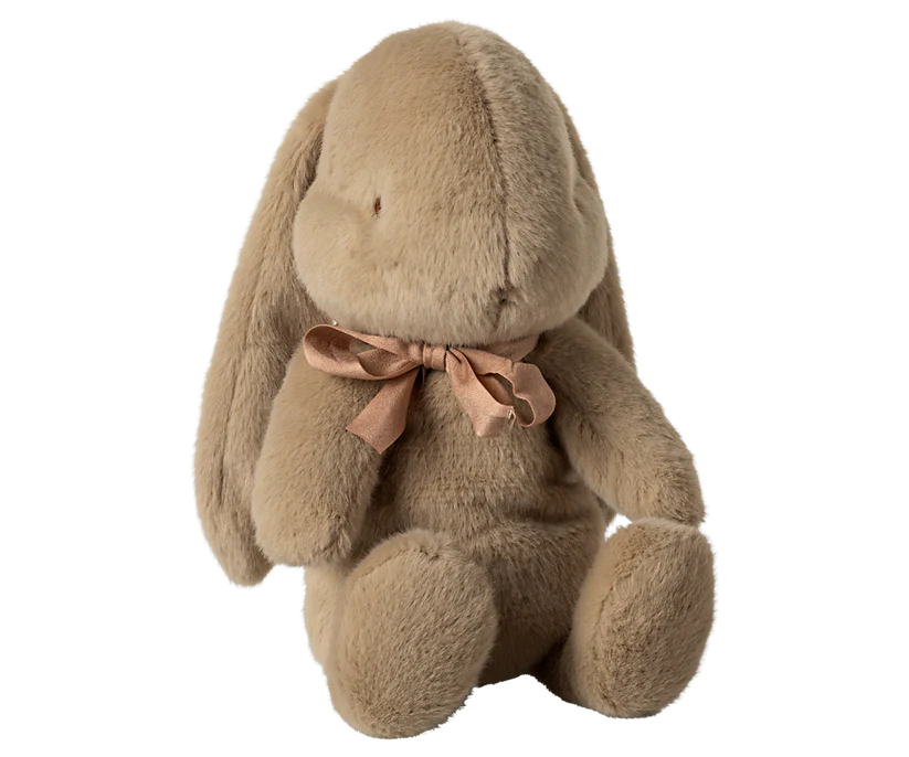 The Maileg Medium Plush Bunny in Dusty Brown features cozy fabric and polyester fillings, designed to sit upright. It boasts long ears and a charming pink ribbon adorning its neck.