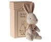 A small, soft grey plush bunny with a brown bow sits in front of a beige box with pink stripes. The gift box features an illustration of a bunny and the words "My First Bunny" along with the brand name "Maileg My First Bunny - Dusty Rose," making it an ideal baby shower gift.