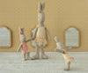 Three Maileg Rabbit, Micro - Ballet Suit and Skirt, Cream stand on a textured surface. Set against yellow patterned wallpaper and three small mirrors, the rabbits are posed like playful ballet dancers in pastel skirts.