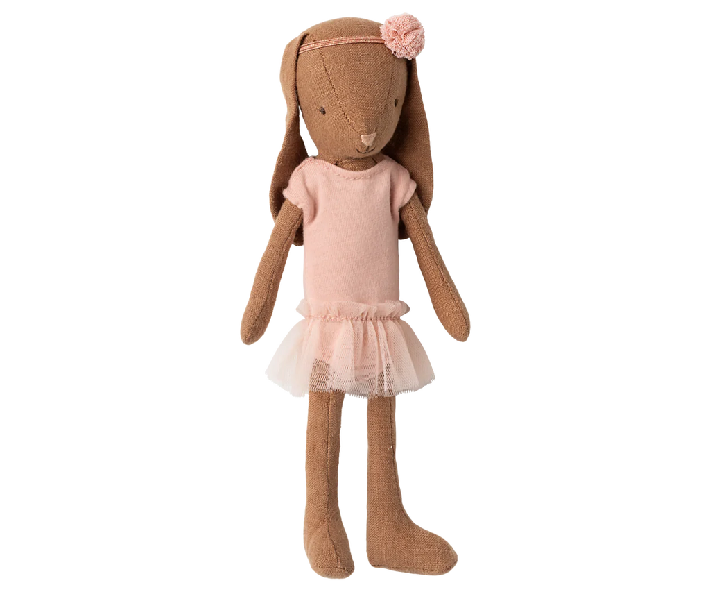 The Maileg Bunny, Size 1, in chocolate brown wears a rose ballet suit and skirt, standing upright like a sweet dancer with a pink flower headband against a blurred background.