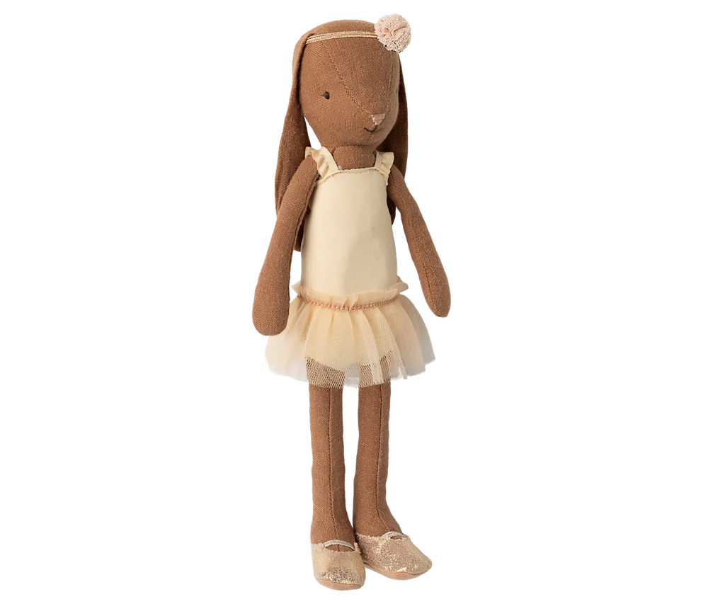The Maileg Bunny, Size 2 in Chocolate Brown, wears a cream ballet suit and skirt and stands upright like a graceful dancer against a blurred background.