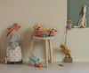 The Maileg Puppy Supply Accessories - Rose features a soft plush dog in a cozy bed atop a stool, with other charming animal toys arranged nearby in a minimal, pastel room for a whimsical, playful display.