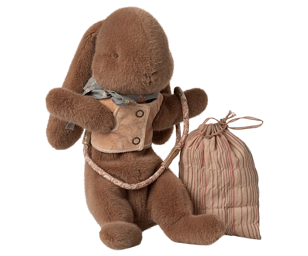 The Maileg Sleeping Bunny Supply, Harness features a plush brown bunny in a tan vest and gray scarf, holding a harness leash set attached to a striped fabric bag.