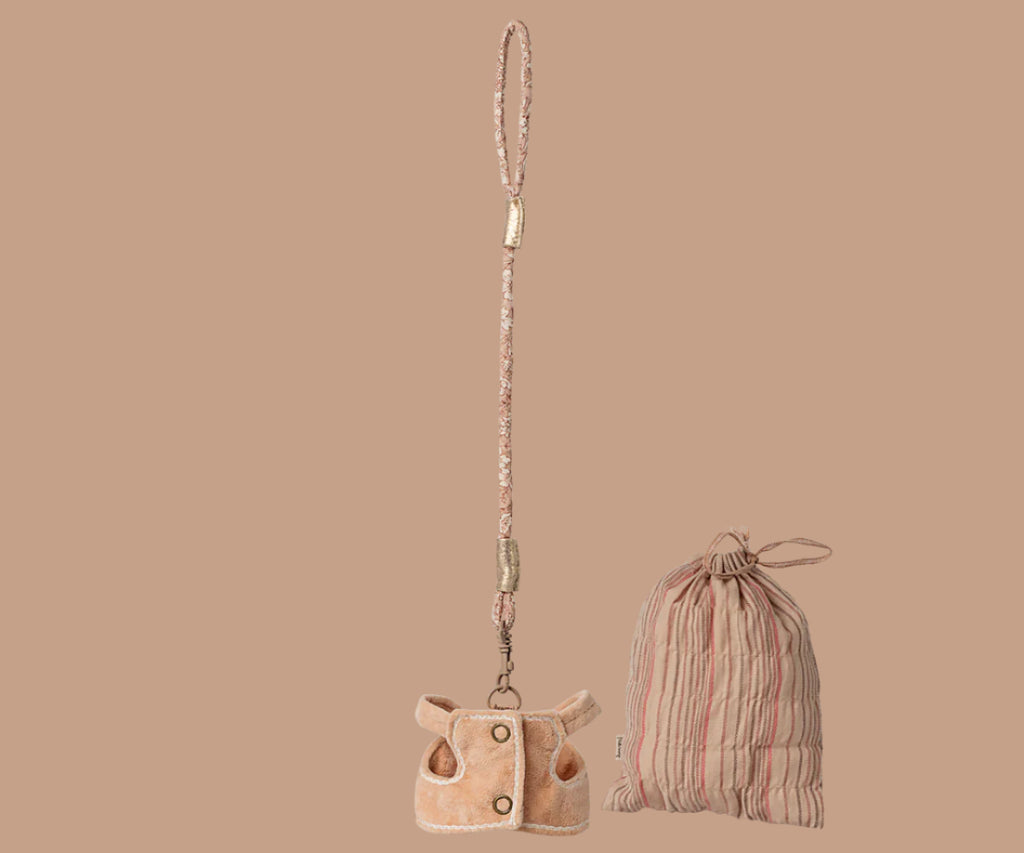 A Maileg Plush Sleeping Bunny With Harness sits with a small beige plush pouch featuring buttons and a patterned strap, plus a pink and beige striped drawstring bag, all displayed on a solid beige background.