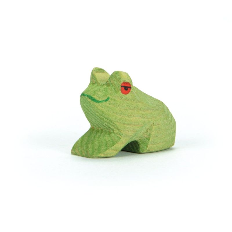 The Ostheimer Frog Sitting is a small wooden figurine painted green, featuring a simple smile and red eyes. It crouches against a plain white background, meticulously handcrafted from sustainably sourced materials. The texture and grain of the wood are clearly visible on its surface.