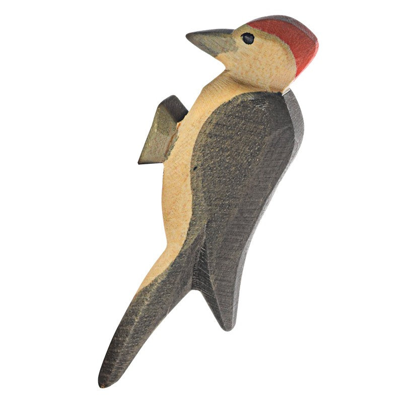 The Ostheimer Woodpecker is displayed as a wooden figurine. This woodpecker features a red cap, dark wings, and beige underparts, closely resembling other Ostheimer toys. The figurine appears to be handcrafted using sustainably sourced materials and is painted with a rustic and textured finish.