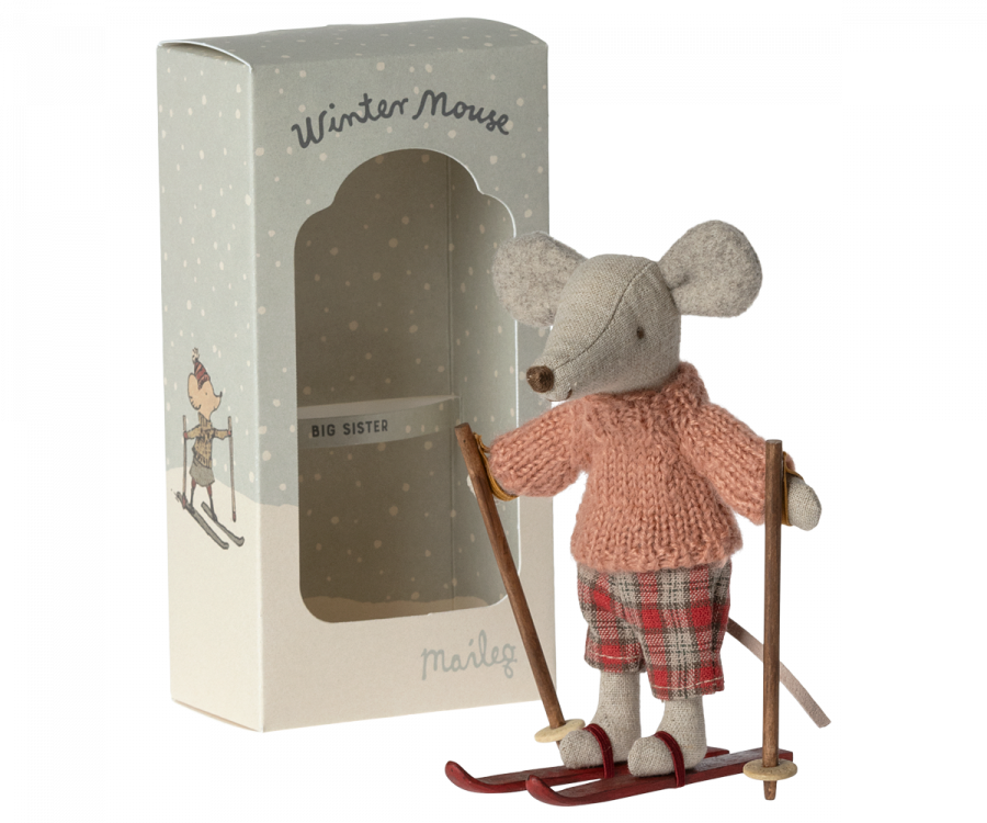 A Maileg Christmas Winter Mouse With Ski Set, Big Sister dressed in a pink sweater and plaid pants is standing on a pair of red skis with ski poles. The mouse is positioned next to its packaging, which reads "Winter Mouse" and "Big Sister" and features an illustration of a mouse skiing. This charming winter toy makes for an adorable Mouse playset.
