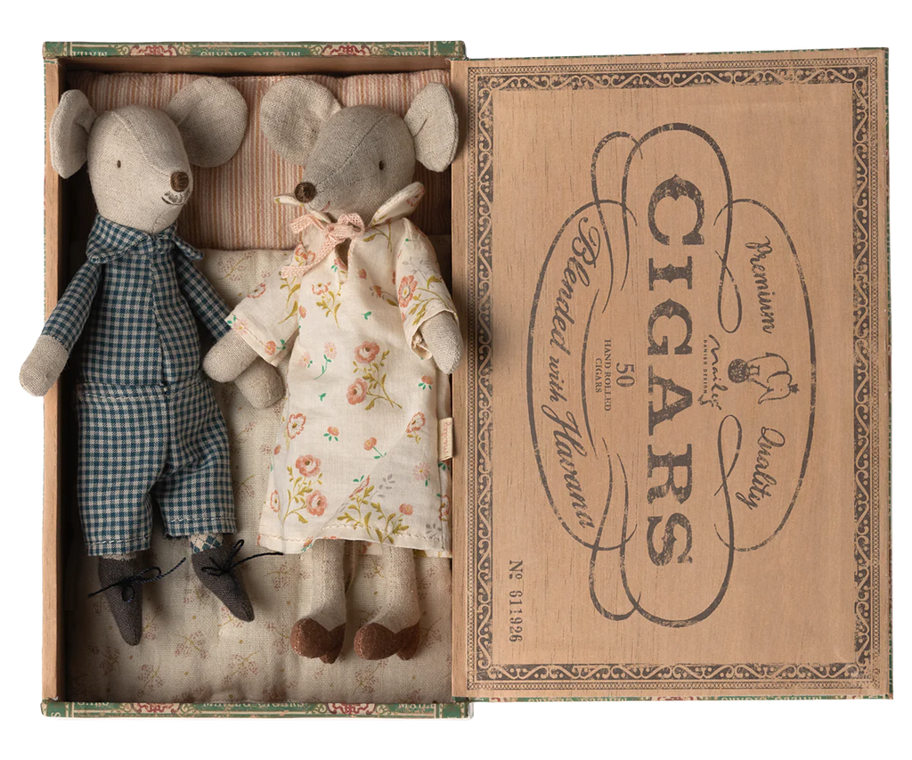 A vintage cigar box repurposed as a display case holds two stuffed mice dolls from the Maileg Set - Sleepover At Grandparents. One mouse is dressed in blue checkered overalls and black shoes, while the other wears a floral dress. The lid of the box features retro-style text and graphics advertising cigars.